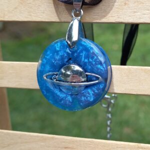 A planet with a single ring surrounded by sapphire blue on a necklace of black cord and black ribbon.