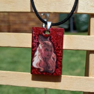 A red female devil with a red russet background on a black faux cord necklace.
