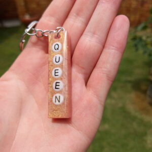 A vertical pink Gold keyring with the word Queen.